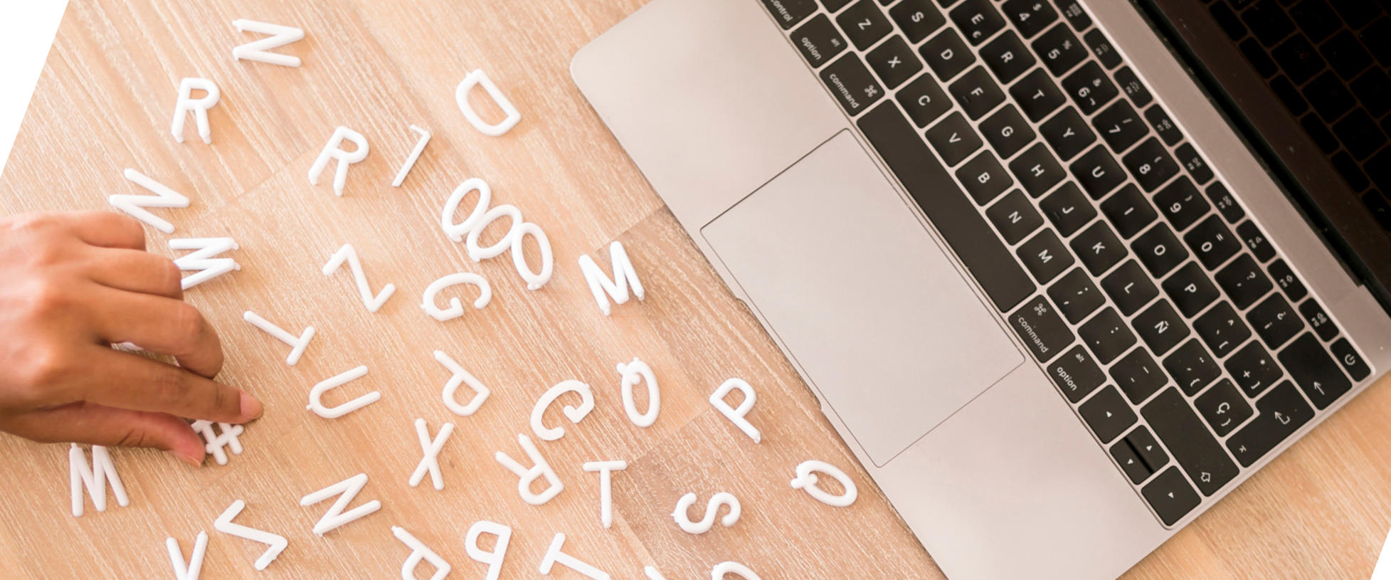 Eine Hand sortiert Plastikbuchstaben, die vor einem Laptop liegen - Symbolbild für einfacher Sprache in der Unternehmenskommunikation