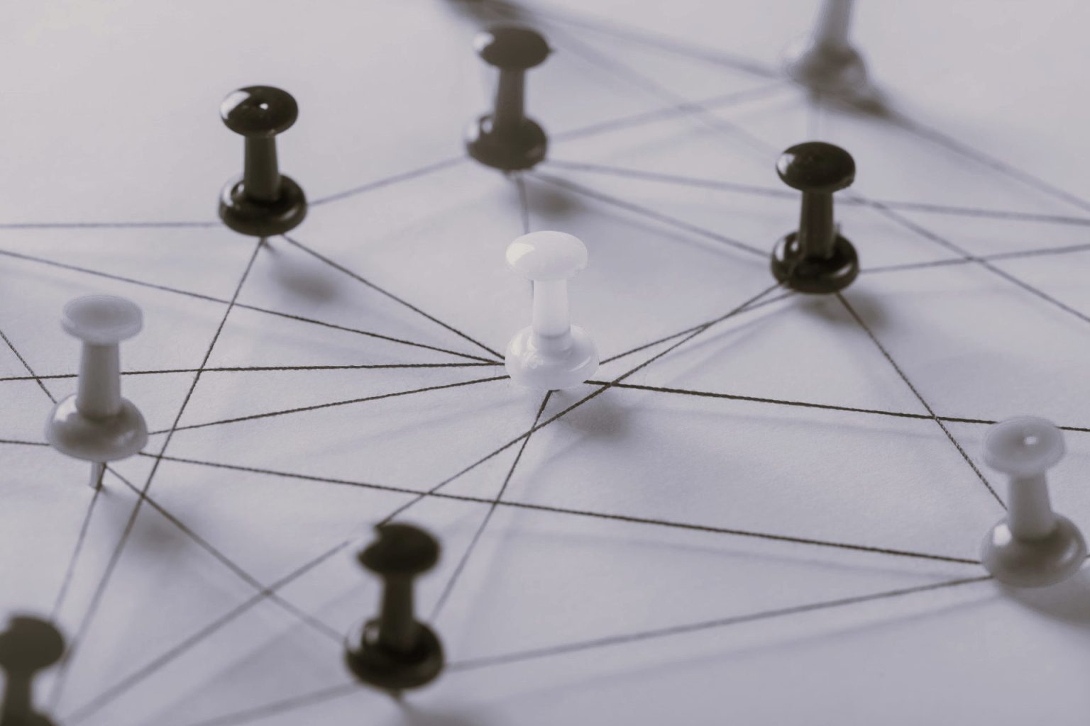 Auf dem Schwarz-Weiß-Foto sind Pinnwand-Pins zu sehen, die durch Fäden miteinander verbunden sind - Symbolbild für Interne Kommunikation