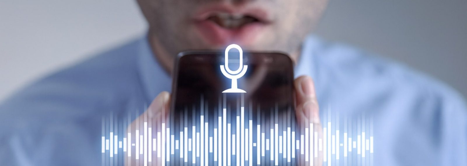Ein Mann im blauen Hemd spricht in ein Handy. Man sieht nur einen Bildausschnitt und eine Grafik mit Mikrophon und Schallwellen liegt über dem Bild. Symbolbild für Voice Search.