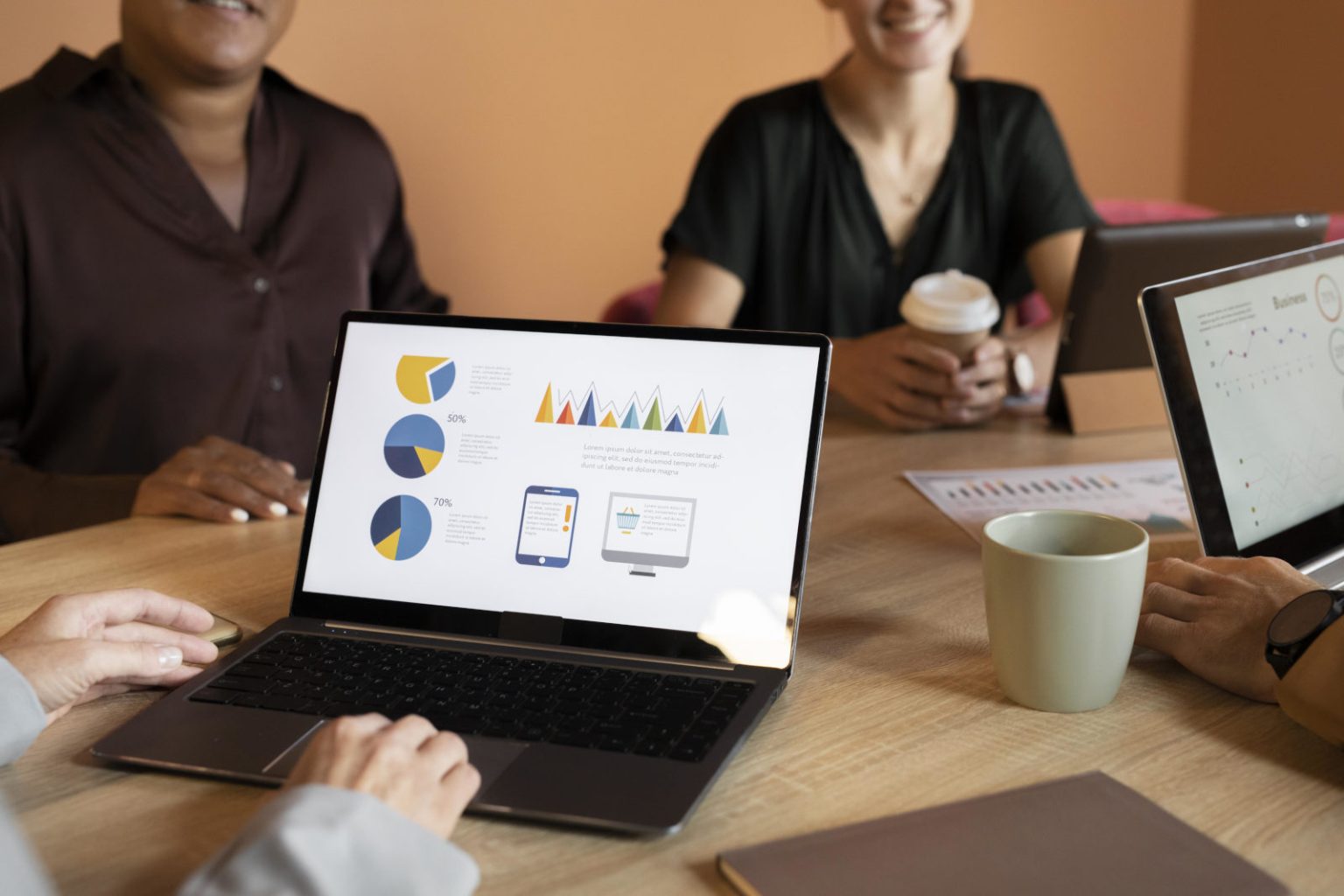 mehrere Personen sitzen an einem Konferenztisch und man sieht Kaffeetassen und einen aufgeklappten Laptop, auf dem ein CRM-Programm zu sehen ist