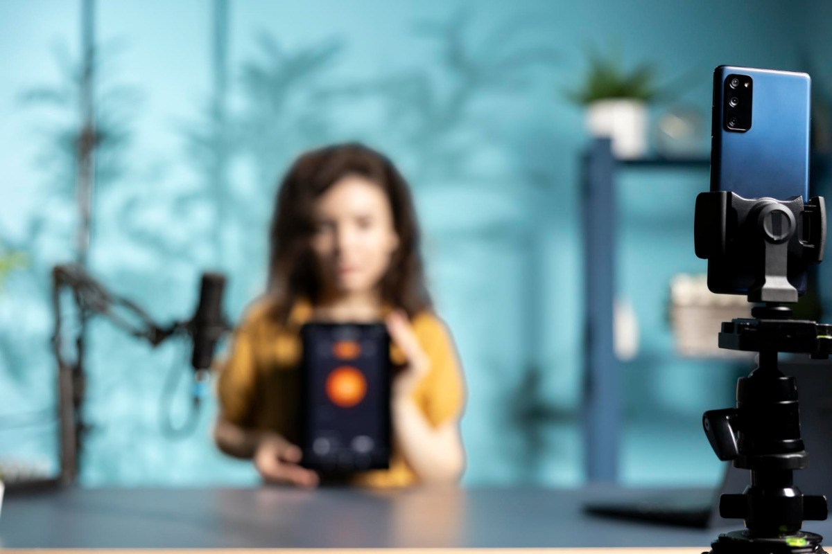 Influencerin sitzt vor einem Handy auf einem Stativ und filmt etwas