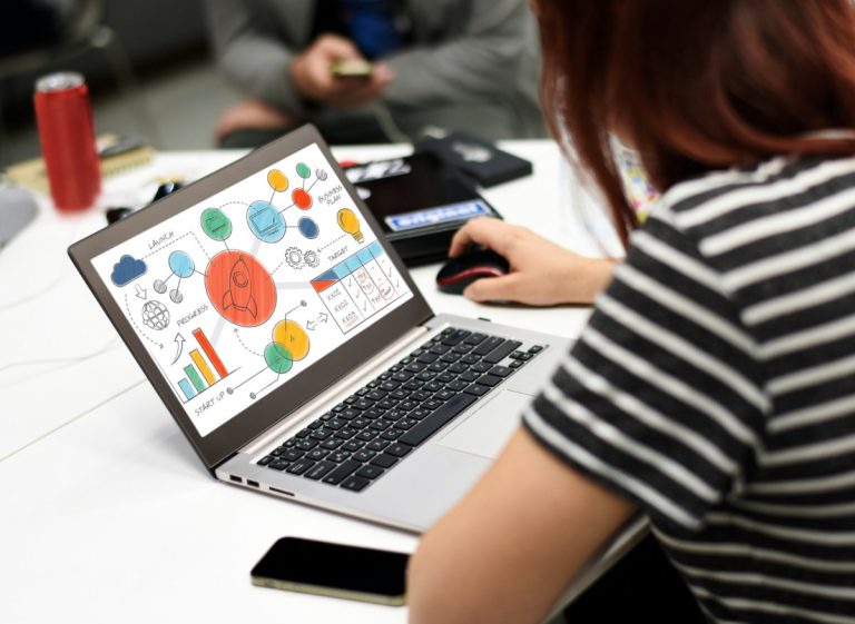 Eine Person sitzt vor einem aufgeklappten Laptop auf dem diverse Analysediagramme zu sehen sind