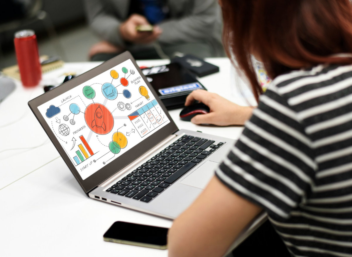 Eine Person sitzt vor einem aufgeklappten Laptop auf dem diverse Analysediagramme zu sehen sind